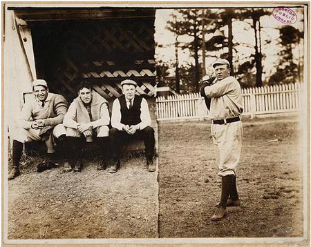 Cy Young posed in pitching motion with three men in dugout watching.